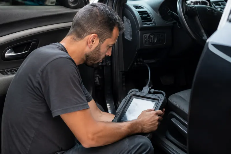 Eletricista com tablet de diagnóstico dentro do carro