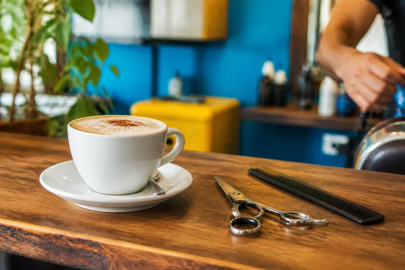 Xícara de cappuccino no balcão ao lado de tesoura e pente