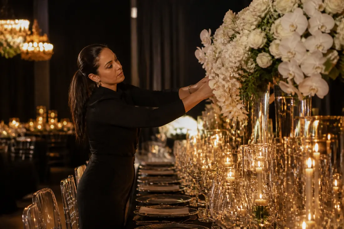 Camila arrumando arranjos de flores brancas em mesa iluminada por velas