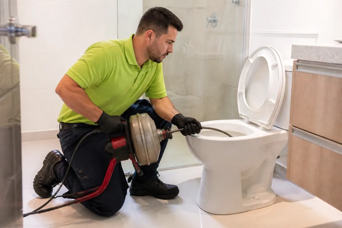 Técnico desentupindo um vaso sanitário com equipamento profissional