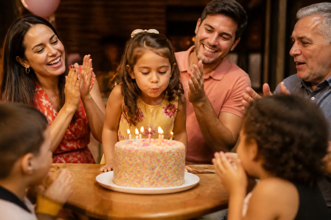 Menina soprando as velas do bolo com a família