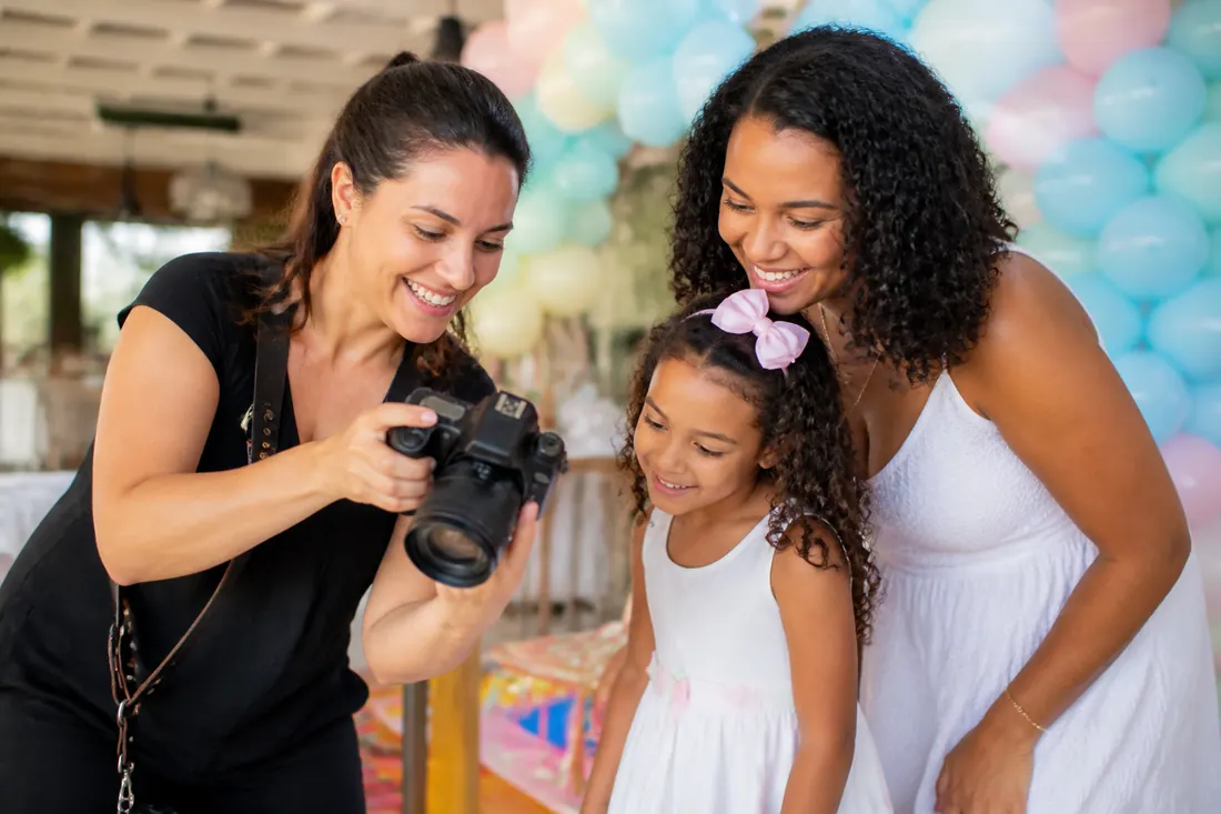 Fotógrafa mostrando as fotos na câmera para mãe e filha