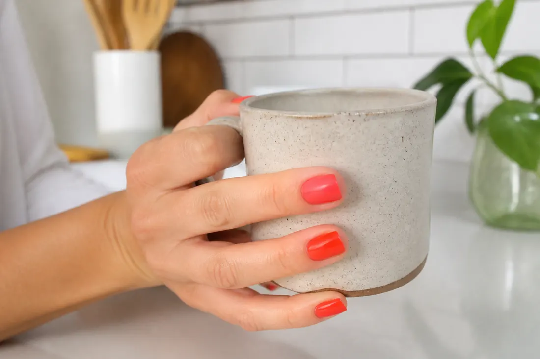 Mão com unhas coral segurando uma xícara